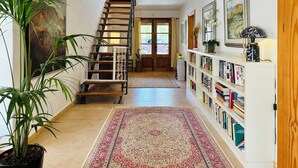 A hallway with a wooden staircase, a bookshelf, and a large potted plant. - Entertainment-packed, Spacious, Peaceful & Convenient (Pollença)