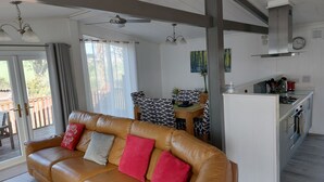 Ein modernes Wohnzimmer mit einer Ledersofa, einem Essbereich mit gemusterten Stühlen und einer Küche mit weißen Schränken und einer Edelstahl-Dunstabzugshaube.