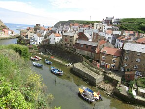 Une ville côtière traversée de canaux étroits bordés de bateaux, où l’on trouve des bâtiments historiques et un pont de pierre.