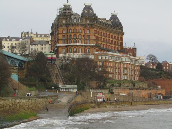 Un edificio grande e histórico de varios pisos con una torre destacada, ubicado cerca de la costa.