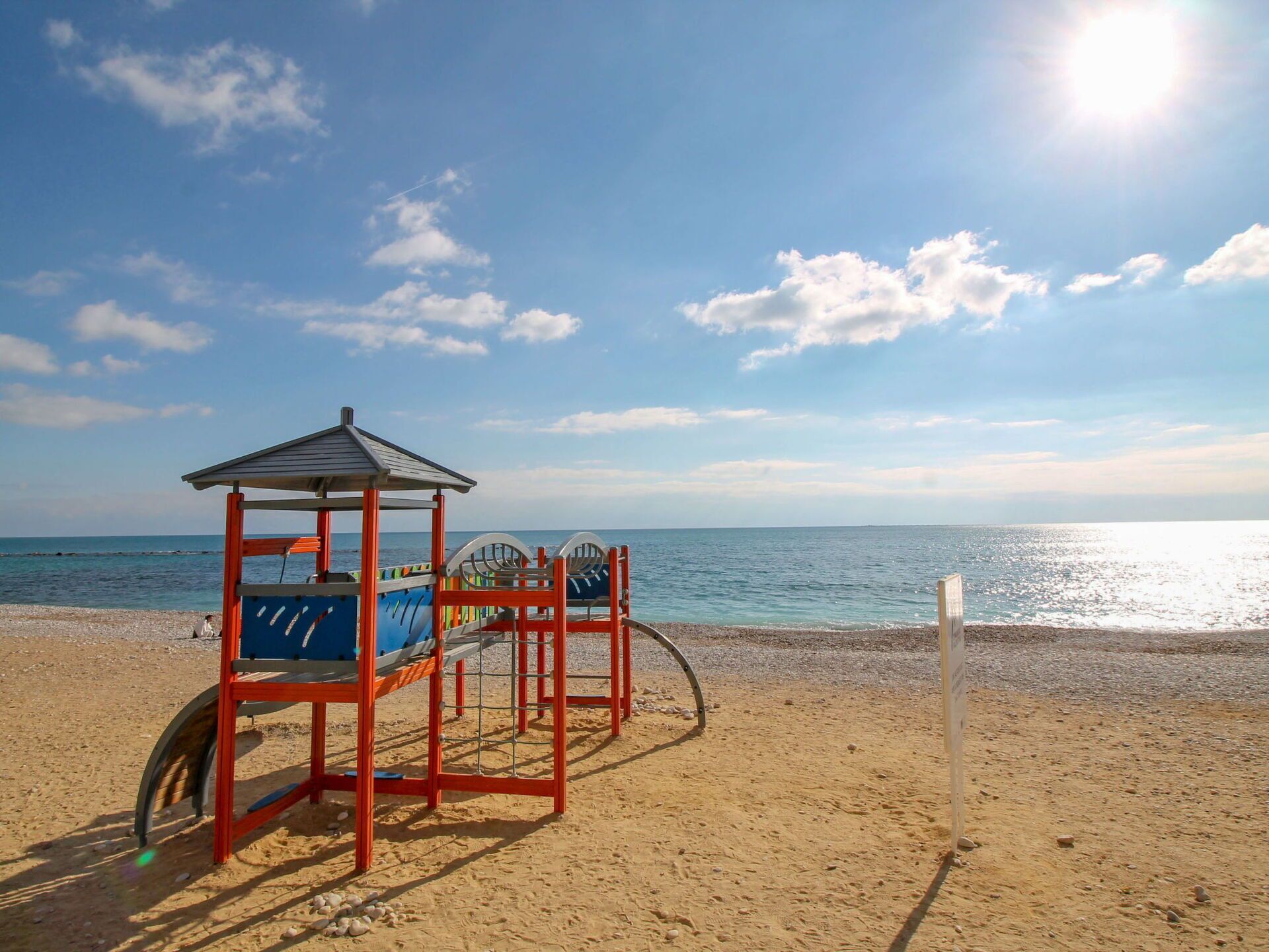 A beach with a children's play structure and a clear view of the sea.