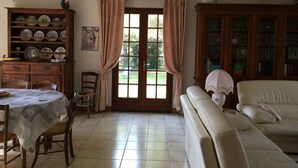 Een woonkamer met een eettafel, stoelen, een bank, een boekenkast en een raam met gordijnen.