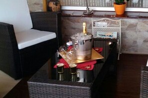 A room with a sofa, a small table with a bottle and glasses, a decorative item, and a potted plant.