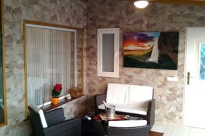 A room with a stone wall, a white door, a painting of a sunset, and a white sofa.
