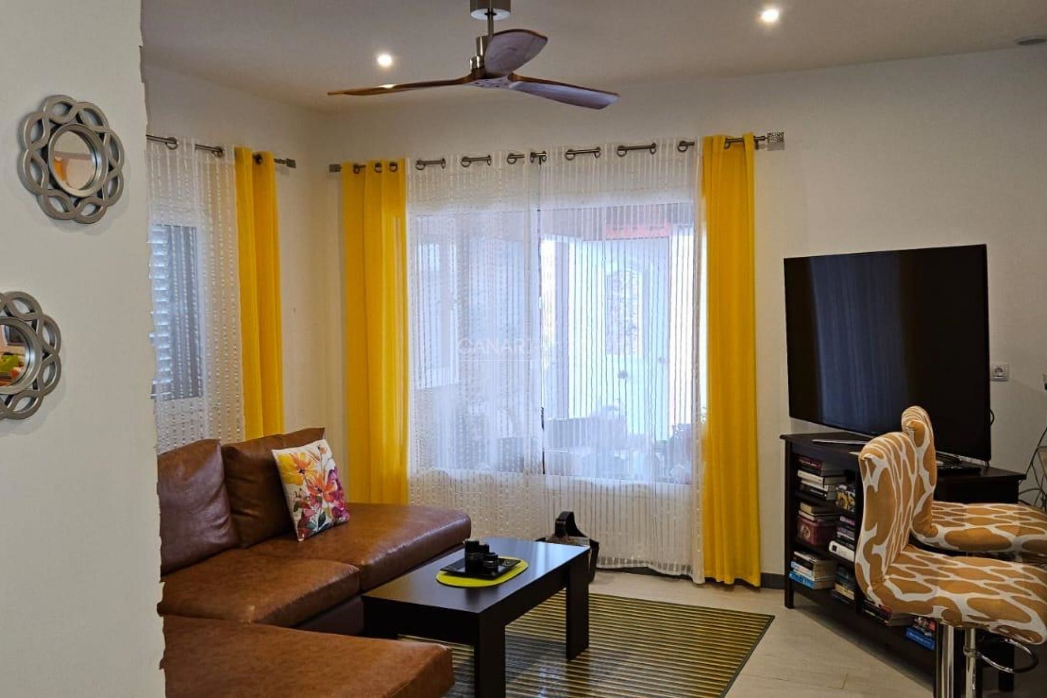 A living room with a sofa, coffee table, TV, and a ceiling fan.