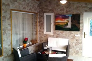Ein Zimmer mit einer Steinwand, einer weißen Tür, einem Sonnenuntergangsbild und einem weißen Sofa.