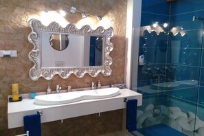Une salle de bain avec un meuble-lavabo blanc, un grand miroir doté d’un cadre orné et une cabine de douche en verre.