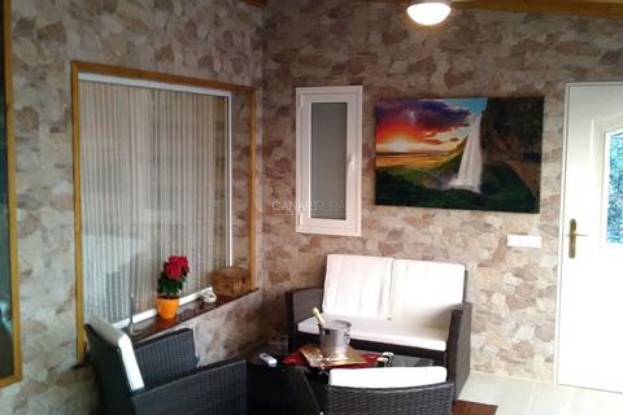 Ein Zimmer mit einer Steinwand, einer weißen Tür, einem Sonnenuntergangsbild und einem weißen Sofa.