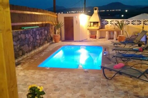 A pool area with lounge chairs, a stone wall, and a door leading to a covered patio. - Stunning New Villa with Private Pool and Terrace in Charming Lajares (La Oliva)