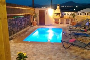 A pool area with lounge chairs, a stone wall, and a door leading to a covered patio.