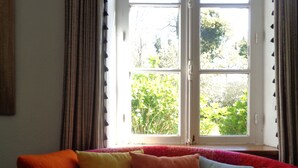 A red sofa with colorful cushions, a window with curtains, and greenery outside. - House with garden (Plobannalec-Lesconil)