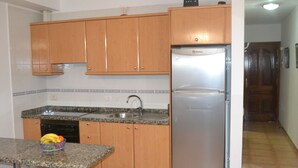 A kitchen with wooden cabinets, a stainless steel refrigerator, a granite countertop, and a sink. - 1 bedroom apartment Las Caletillas (Las Caletillas)