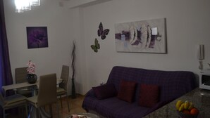 A living room with a purple sofa, a dining table with chairs, and a fruit bowl on the counter. - 1 bedroom apartment Las Caletillas (Las Caletillas)