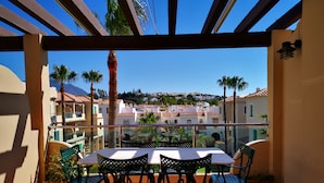 A balcony with a table and chairs, overlooking a coastal town with buildings and palm trees. - Beach Diamond - fantastic duplex right on the beach close to everything (Marina de Casares)