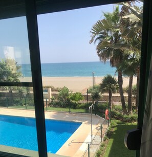 Vue sur une piscine et une plage, prise de l’intérieur d’un bâtiment.