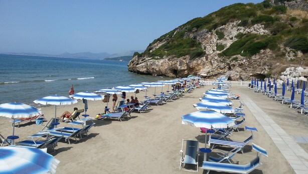 A beach with rows of sun loungers and umbrellas, a rocky cliff in the background, and the sea in the distance. - Apartment in Villa Valentini, Seafront, Gulf of Gaeta parking included (Minturno)