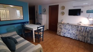 A compact living space with a sofa, dining table, chairs, a kitchen area with a refrigerator, and a TV mounted on the wall. - Apartment in Villa Valentini, Seafront, Gulf of Gaeta parking included (Minturno)