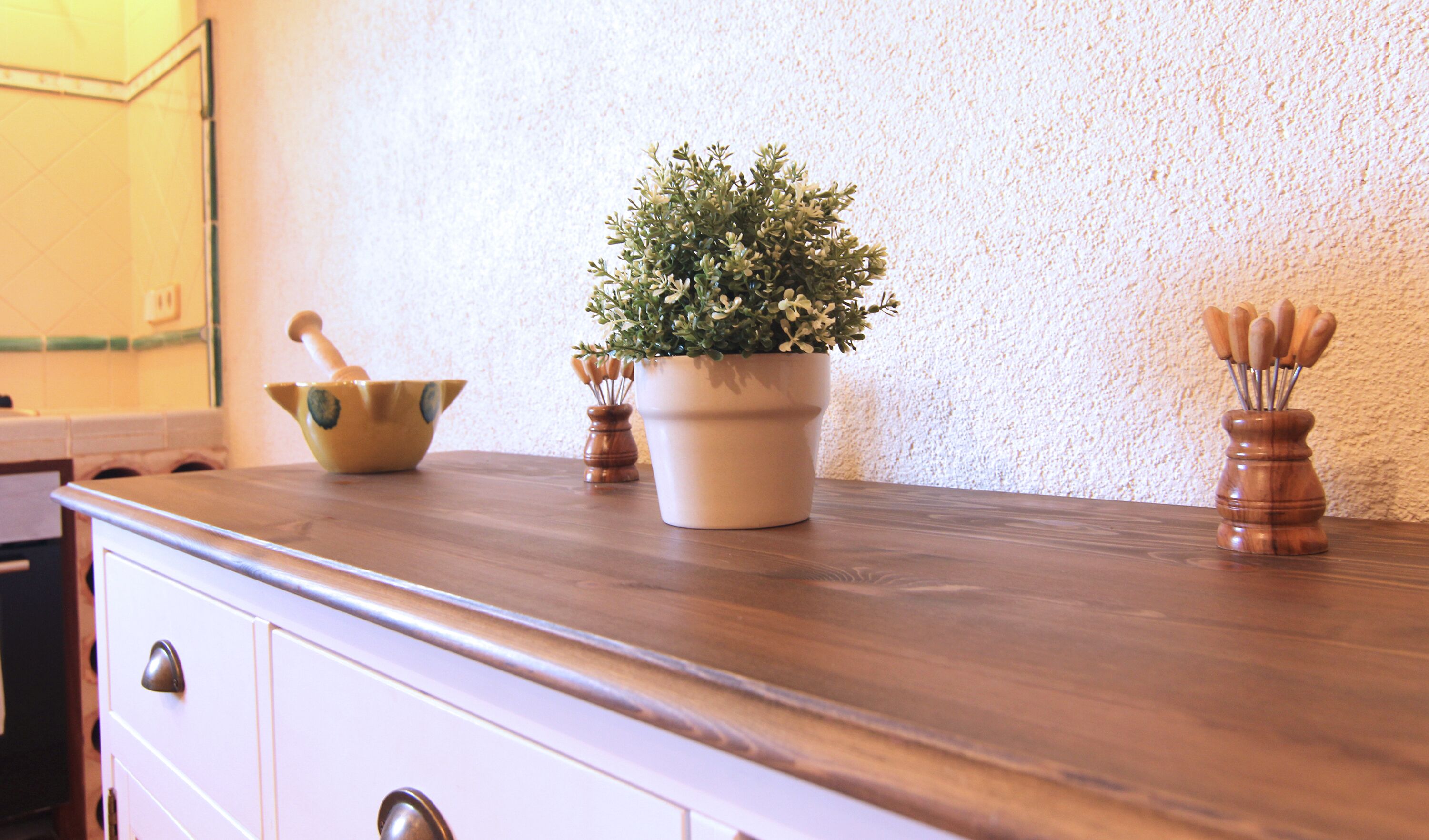 A kitchen counter with a potted plant, a wooden bowl, and a wooden utensil holder.