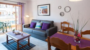 A modern living room with a grey sofa, a dining table with chairs, a wooden dining table, and a view of the outside balcony.