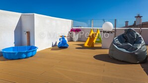 A rooftop terrace with a blue plastic tub, a yellow slide, a blue scooter, and a gray bean bag.