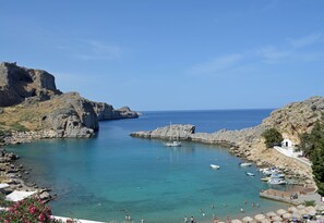 A coastal area with rocky terrain, clear blue water, boats, and a small building with a white roof. - Beautiful Tranquil 3 bed 2 bath Villa with large Private pool 5 min from Lindos (Rhodes)