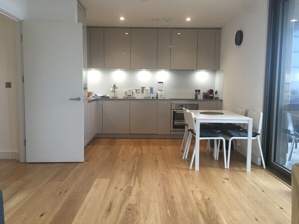 A modern kitchen with grey cabinets, a white countertop, and a dining area with a table and chairs. - LUXURY SERVICED APARTMENTS***** (Croydon)