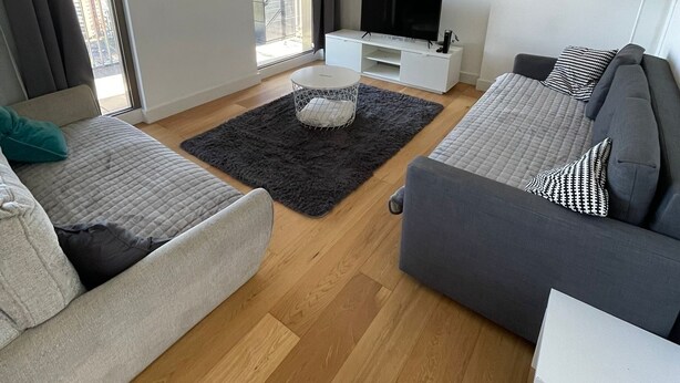 A modern living room with a grey sofa, a white side table, a black rug, and a TV on a white stand. - LUXURY SERVICED APARTMENTS***** (Croydon)
