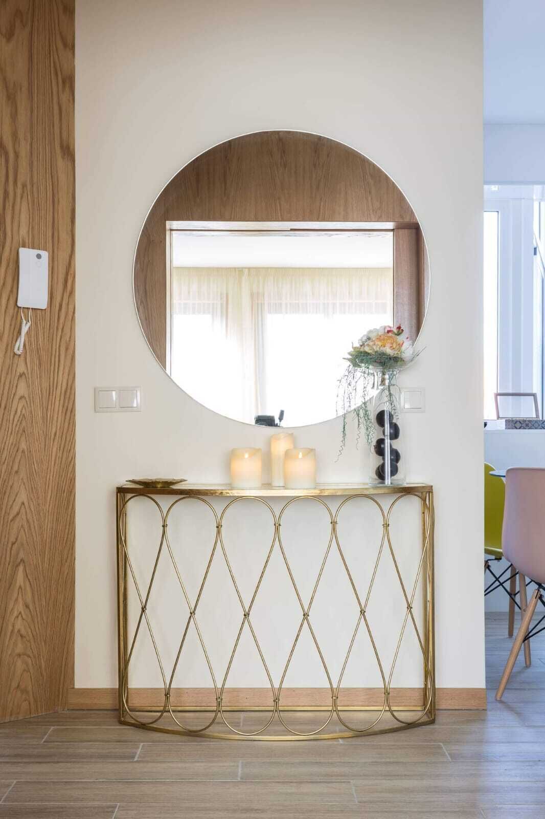 A round mirror above a console table with candles and a vase of flowers.