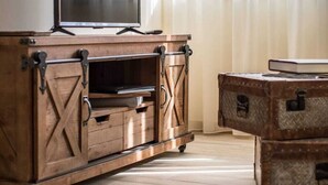 A wooden entertainment unit with a flat-screen TV, drawers, and a suitcase. - Invicta Soul Joy (Porto)