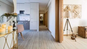 A modern kitchen with white cabinets, a dining area with a pink chair, and a wooden floor. - Invicta Soul Joy (Porto)