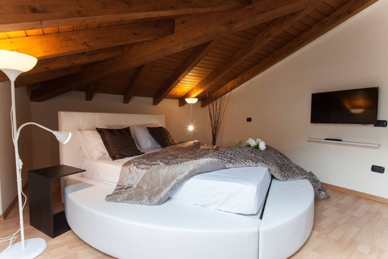 Une chambre moderne avec un lit aux lignes courbes, un téléviseur à écran plat et un plafond en bois.