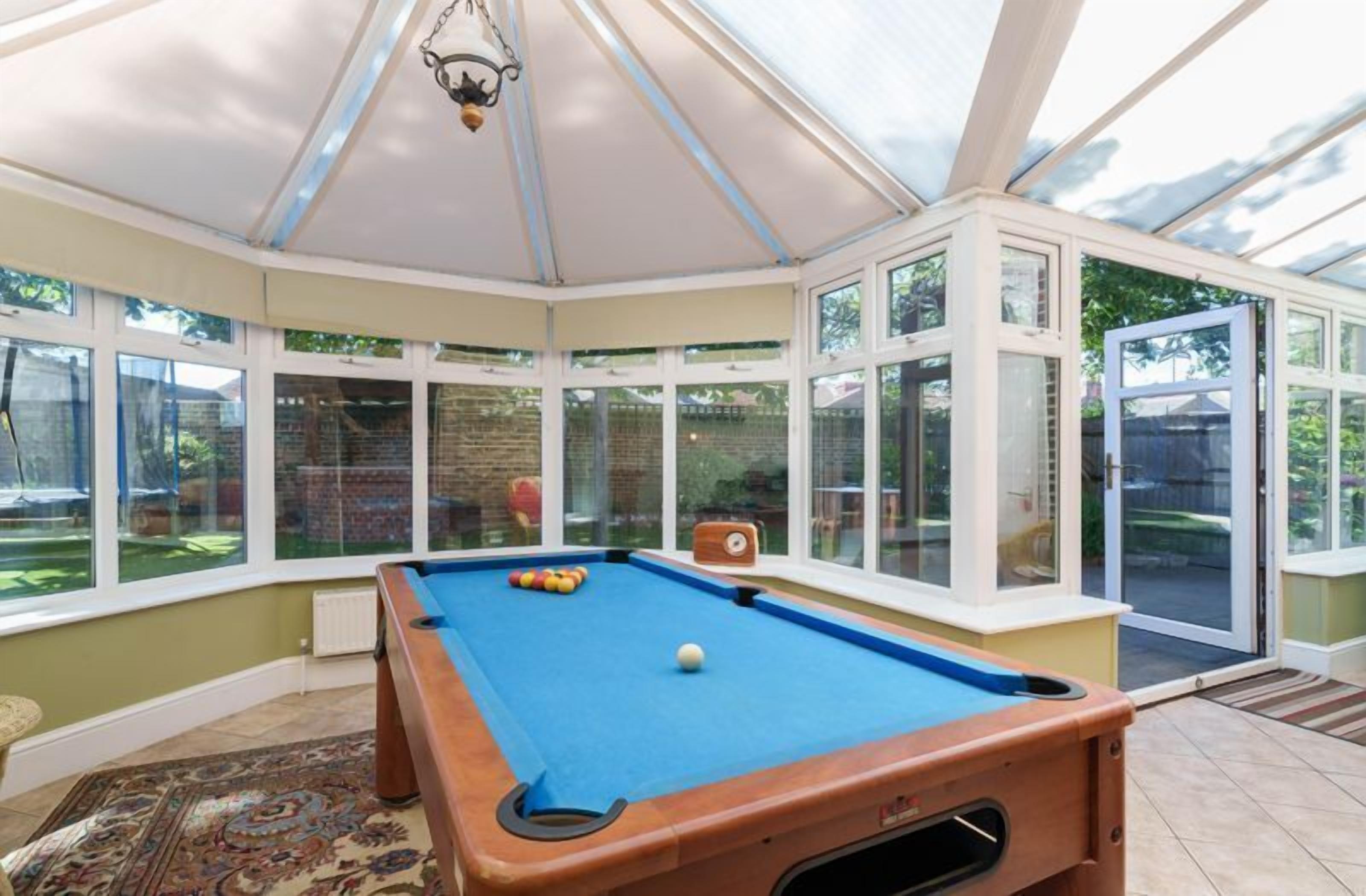A pool table in a conservatory with large windows and a door leading outside.