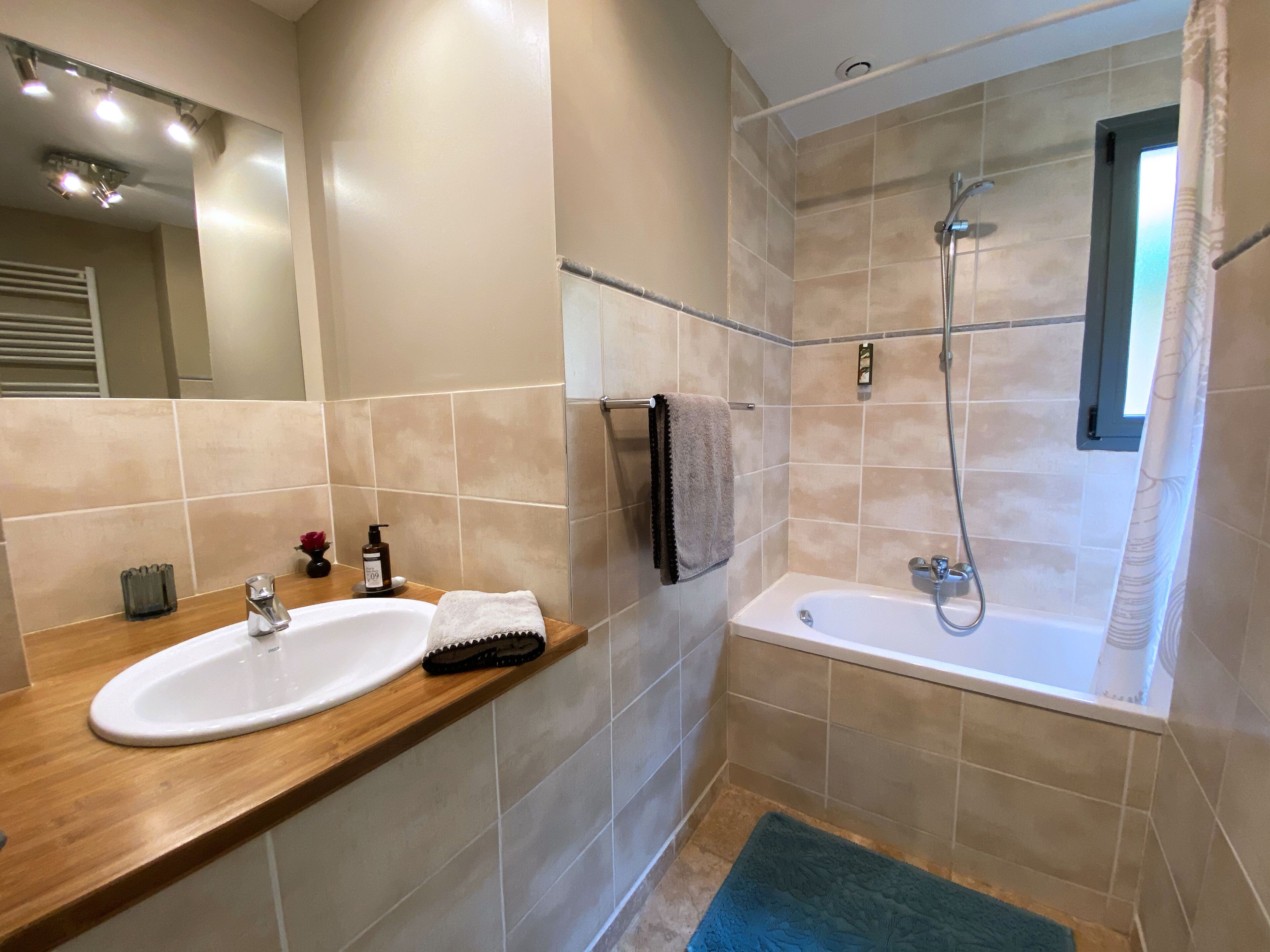 A modern bathroom with a wooden vanity, a white sink, a towel rack, and a shower area with a glass door.