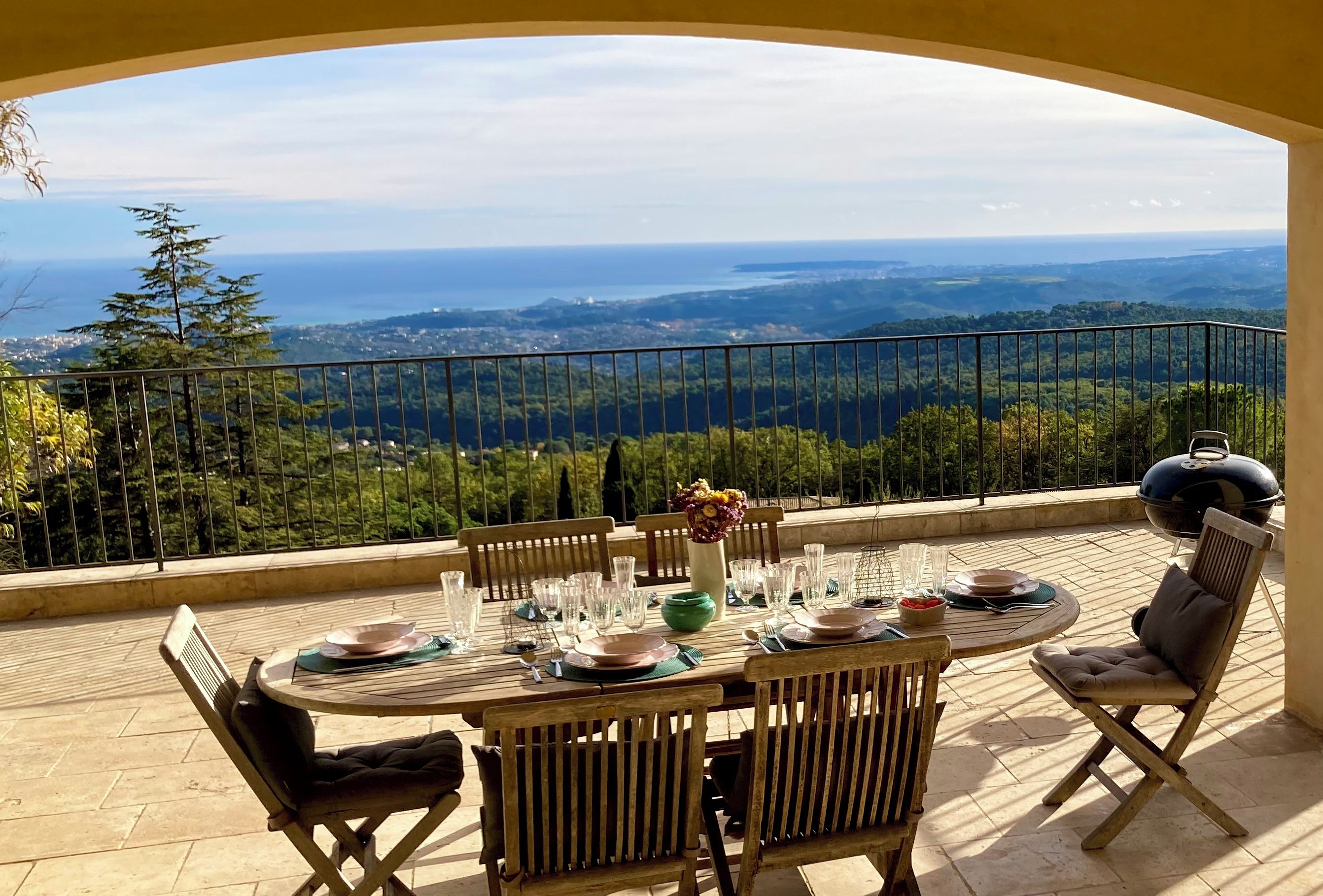 A dining area with a table set for four, overlooking a scenic landscape with trees and a view of the sea.