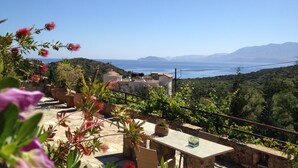 A terrace with a stone table, potted plants, and a view of the sea and mountains.