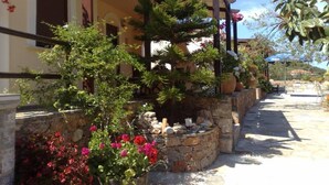 A stone pathway leading to a building with a covered porch area, surrounded by various potted plants and flowers.