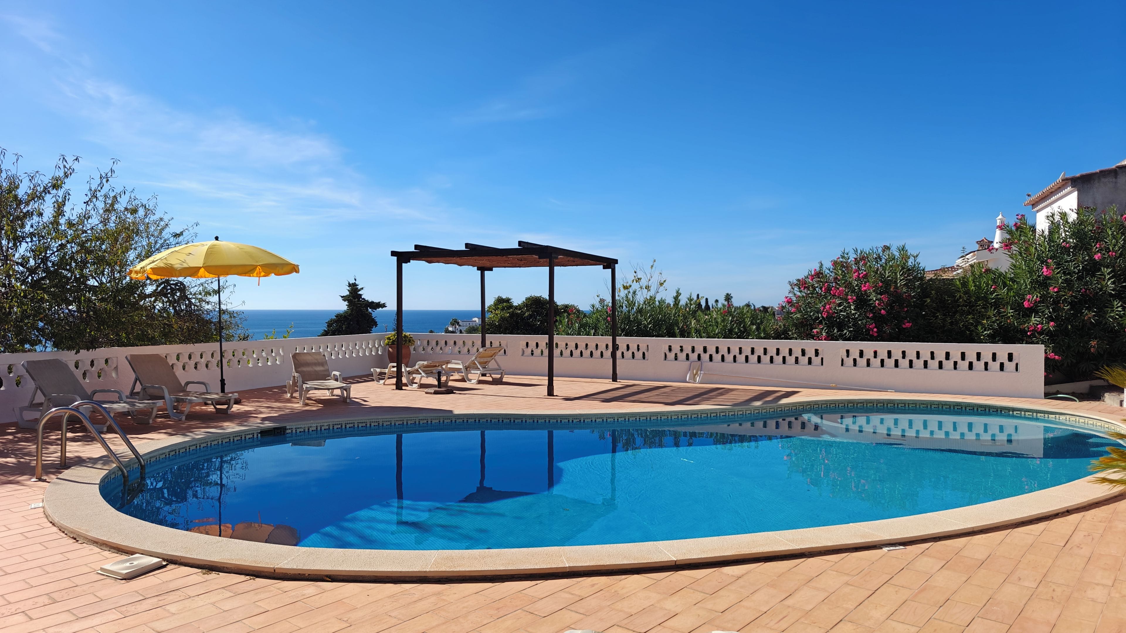 A swimming pool with lounge chairs and a pergola, overlooking a body of water.
