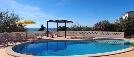 A swimming pool with lounge chairs and a pergola, overlooking a body of water.