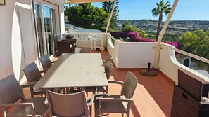 An outdoor patio with a table and chairs, a grill, and a view of a hilly landscape.