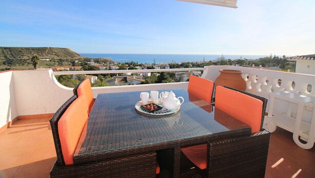 Ein Balkon mit Tisch, der für Tee gedeckt ist, Korbstühlen und Blick aufs Meer.