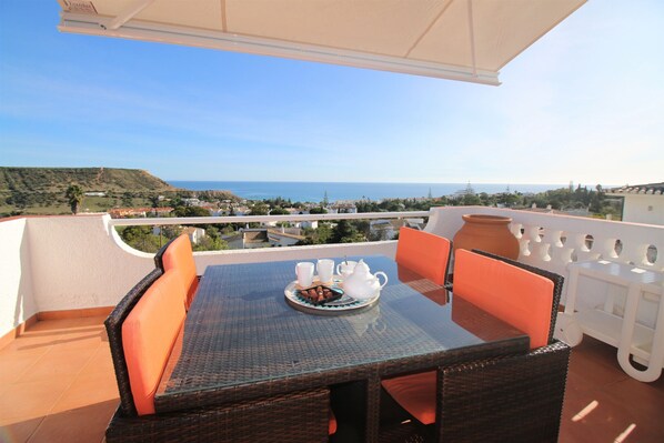 Ein Balkon mit Tisch, der für Tee gedeckt ist, Korbstühlen und Blick aufs Meer.