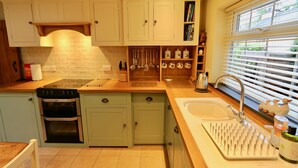 A kitchen with light green cabinets, a built-in oven, a sink with a dish rack, and a window with blinds.