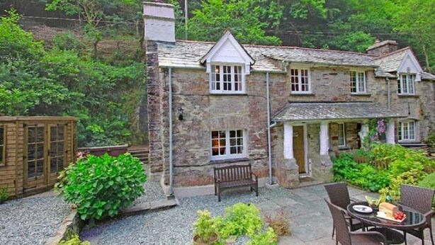 A stone house with a garden patio, a wooden fence, and a bench.
