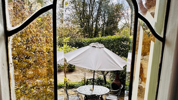 Ventana con vista a un patio que cuenta con una mesa, sillas, un paraguas blanco y un camino de piedra.