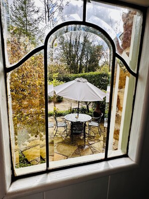 Ventana con vista a un patio que cuenta con una mesa, sillas, un paraguas blanco y un camino de piedra.