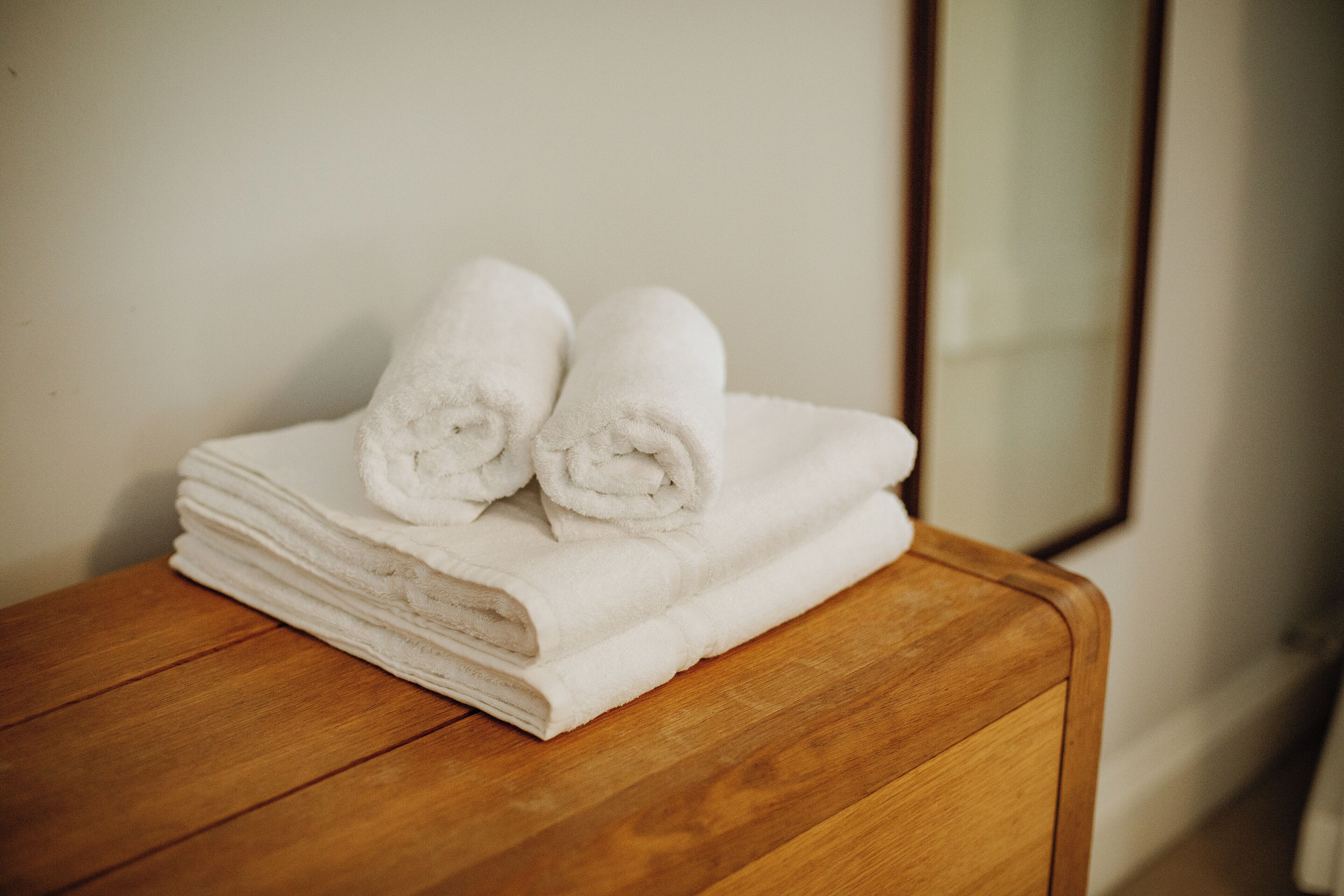 A stack of white towels on a wooden table in a room with a mirror on the wall.