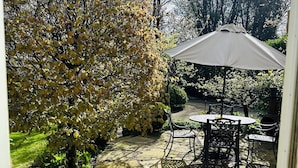 Un patio con una mesa y sillas, rodeado de macetas con plantas y un gran paraguas.