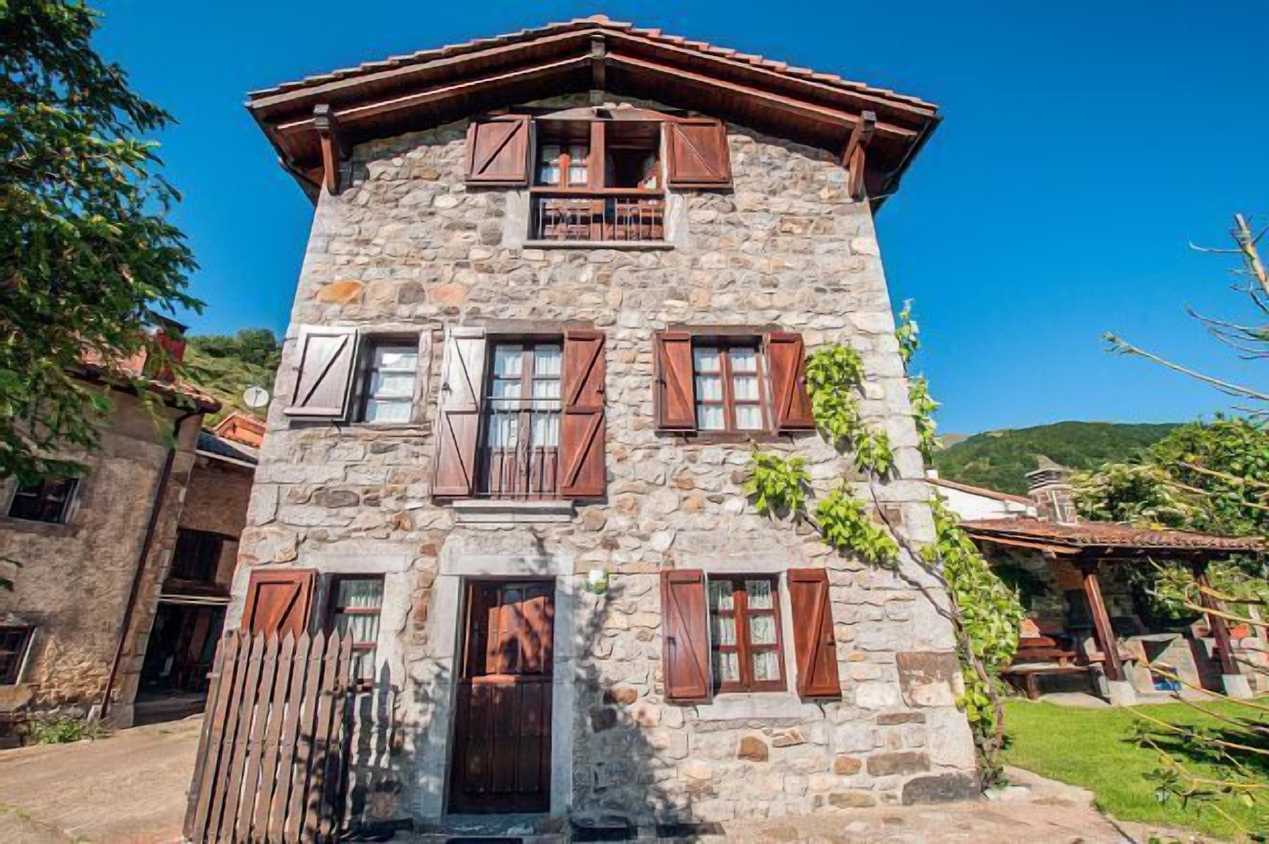 Ein Gebäude aus Stein mit einem Balkon, Holjalousien und einer Tür.