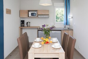 Een moderne keuken met een magnetron, koffiezetapparaat en vaatwasser. Er is een eettafel met stoelen en een bloevas.