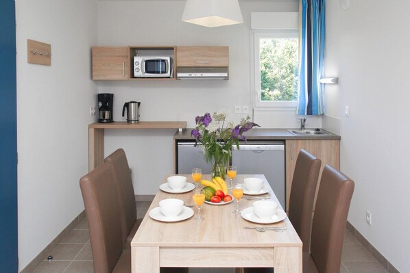 A modern kitchen with a microwave, coffee maker, and dishwasher. There is a dining table with chairs and a vase of flowers.